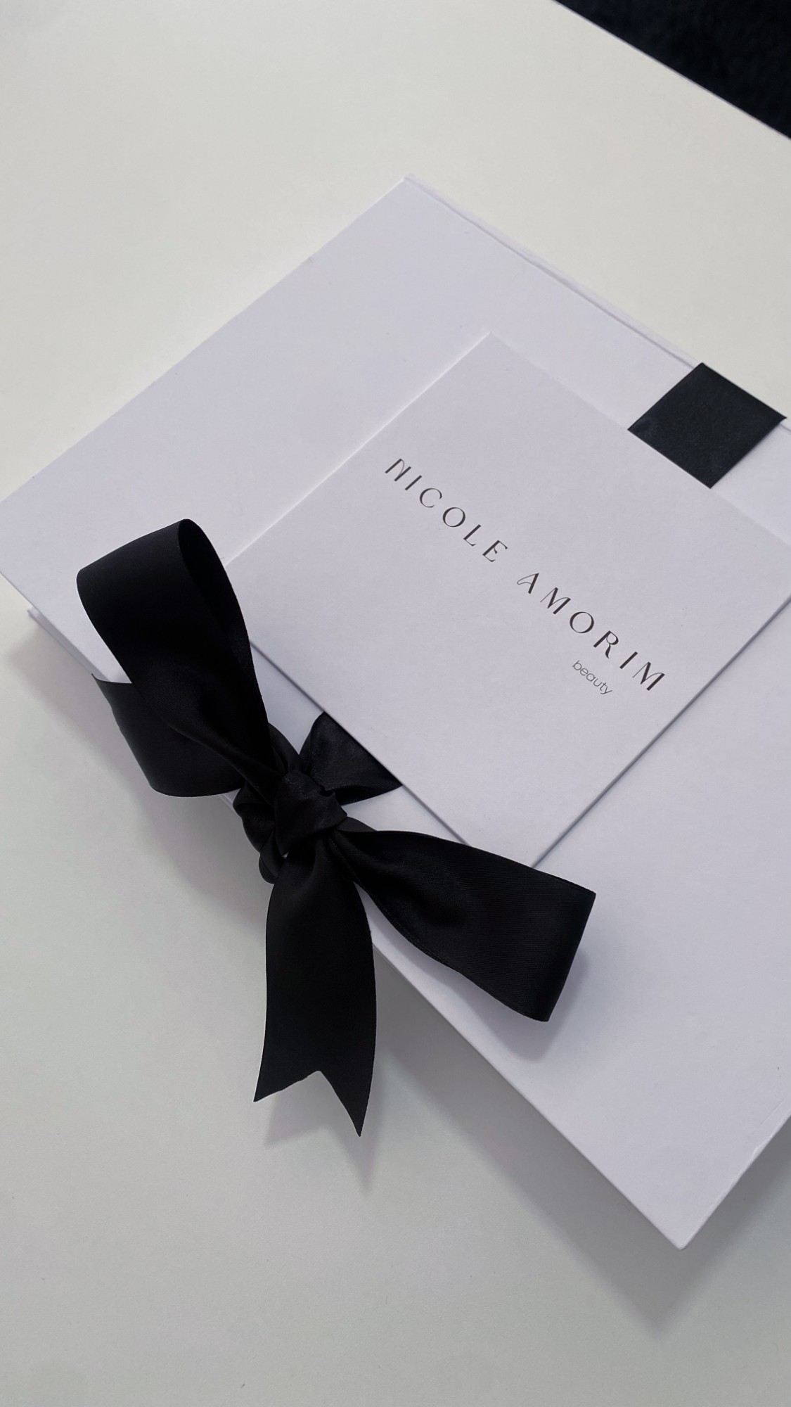Kit do curso: caixa branca com laço preto e a marca Nicole Amorim beauty